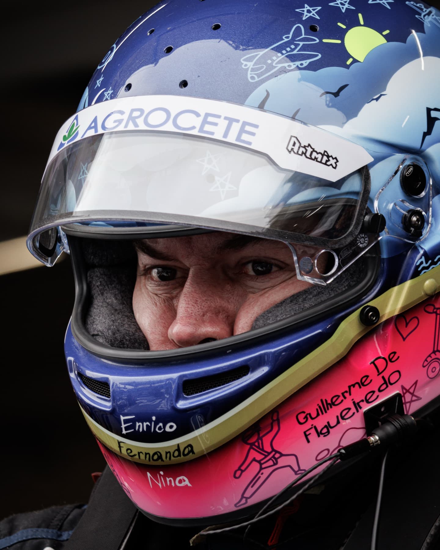 Close do capacete de Guilherme Figueiredo: desenhos infantis de nuvens, sol e avião, os nomes da família escritos à mão e uma faixa dourada na lateral.