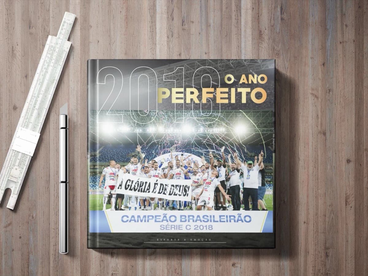 Almanaque do Operário 2018 fechado sobre uma mesa de madeira, com a capa 'um ano perfeito' e a foto da equipe erguendo o troféu.