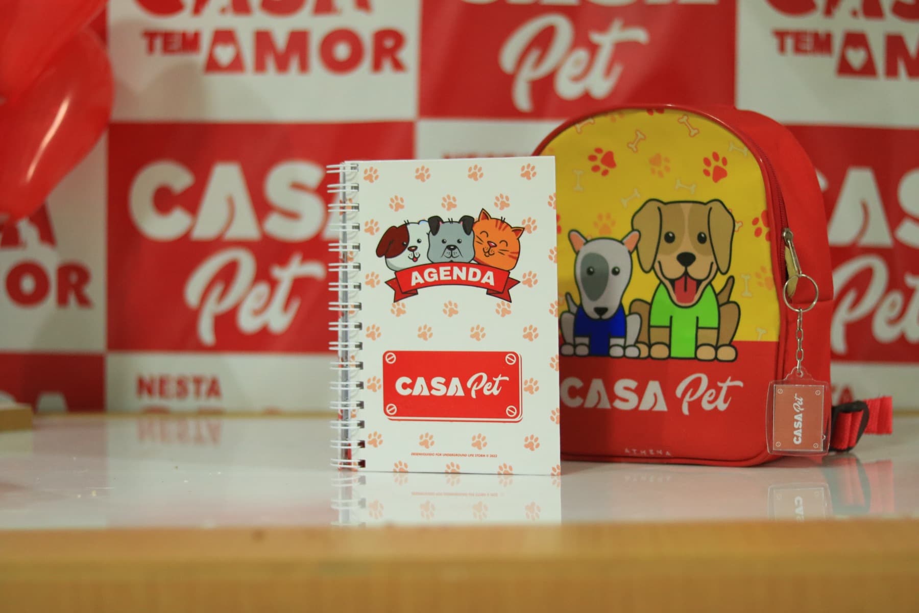 Agenda e mochila da Casa Pet sobre a mesa, em frente ao painel vermelho da creche