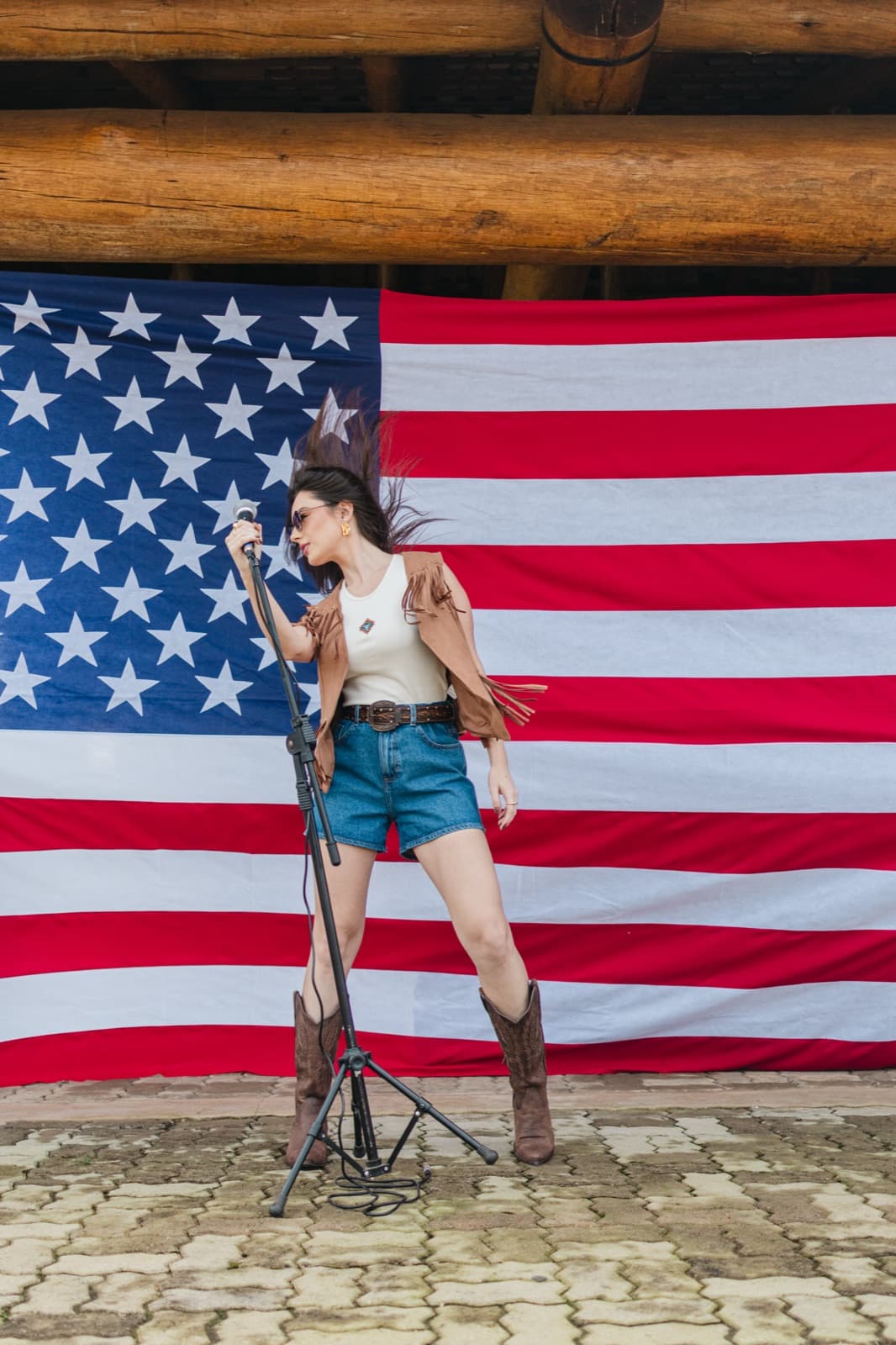 Demy Manosso de corpo inteiro ao pedestal do microfone, com a bandeira americana ao fundo