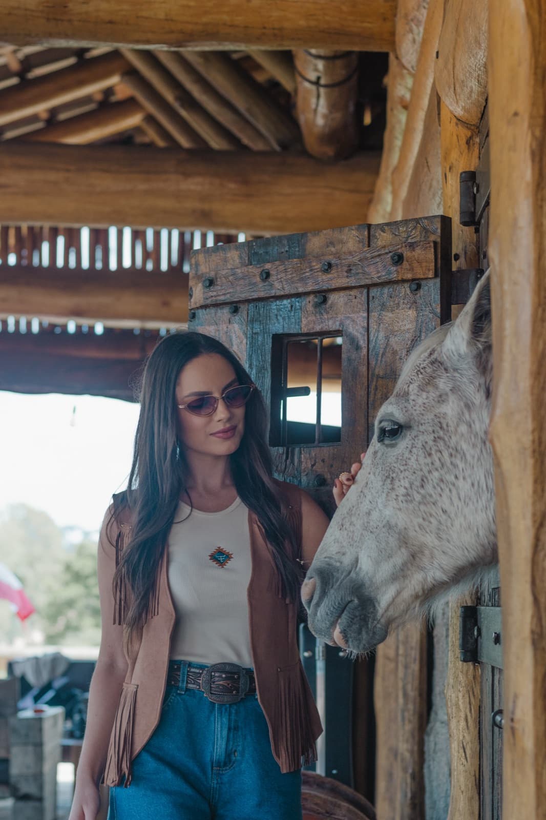 Demy Manosso de óculos ao lado de um cavalo branco que olha pela baia