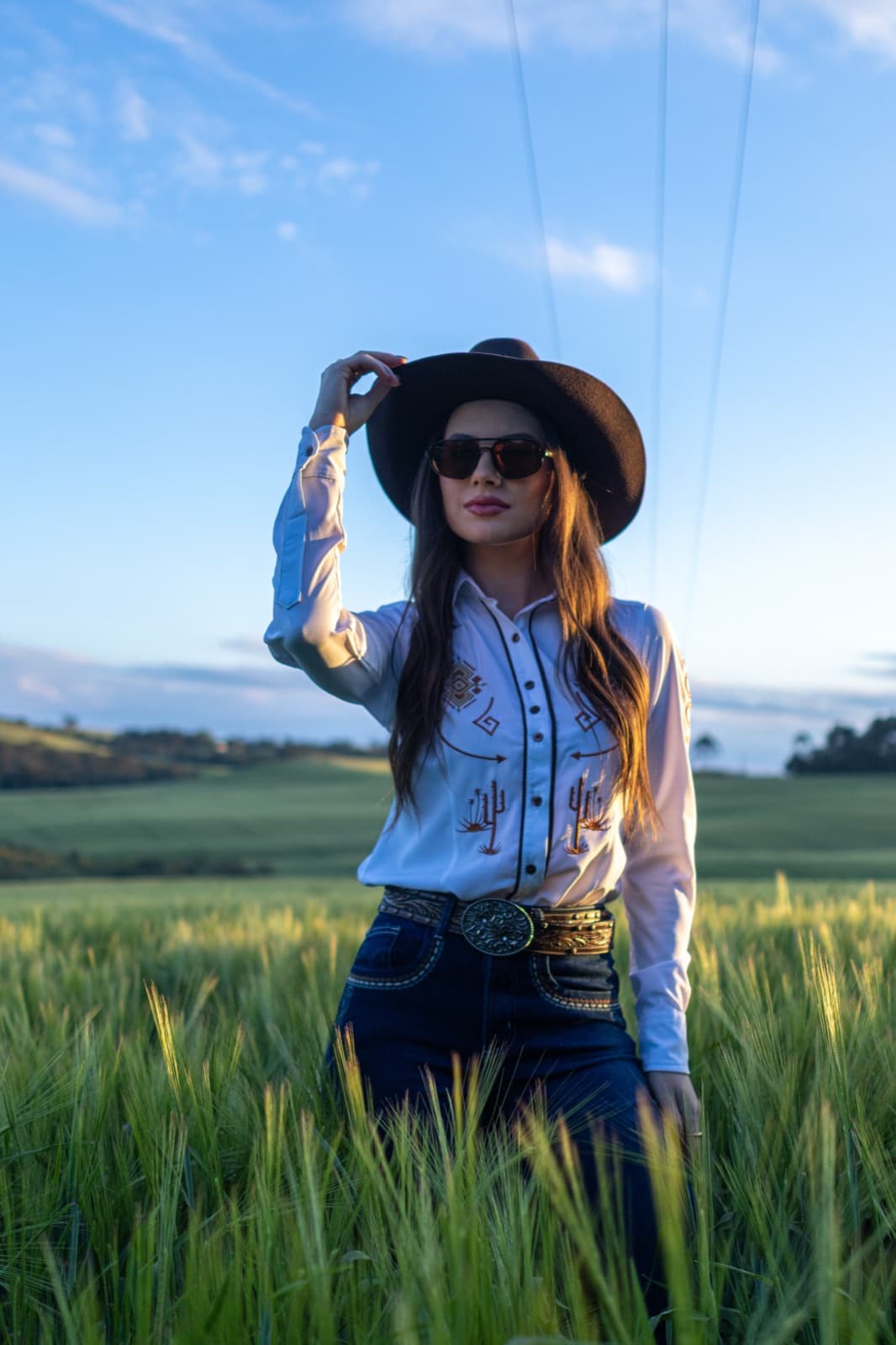 Demy Manosso de chapéu e óculos escuros no meio de um trigal sob céu azul