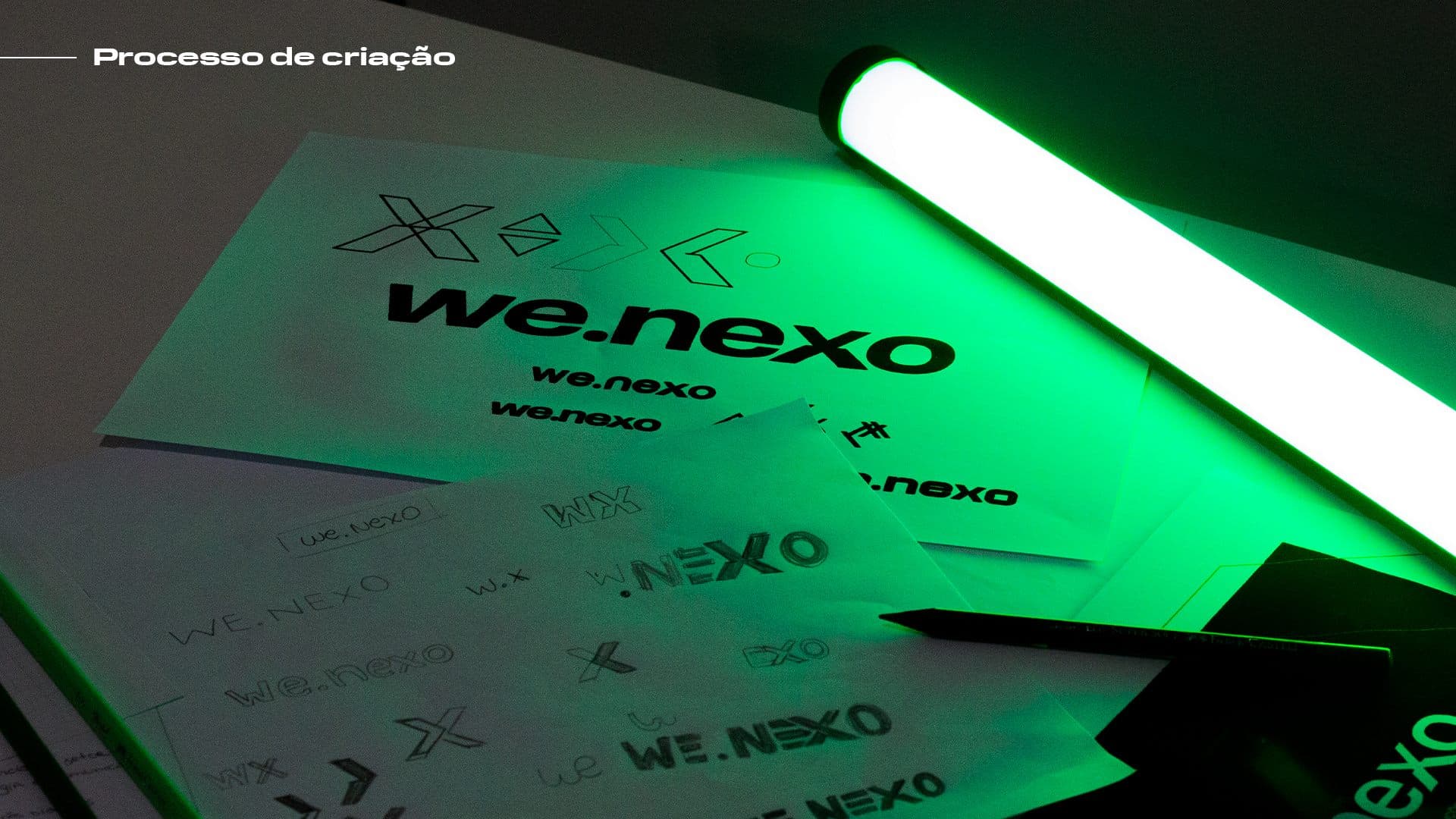 Sketches do logo we.nexo em papel, iluminados por luz LED verde